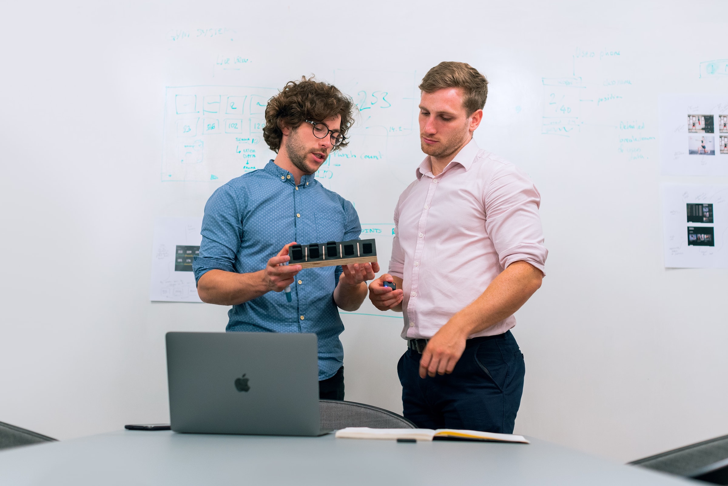 Two men in an office discussing and reviewing a tech prototype.