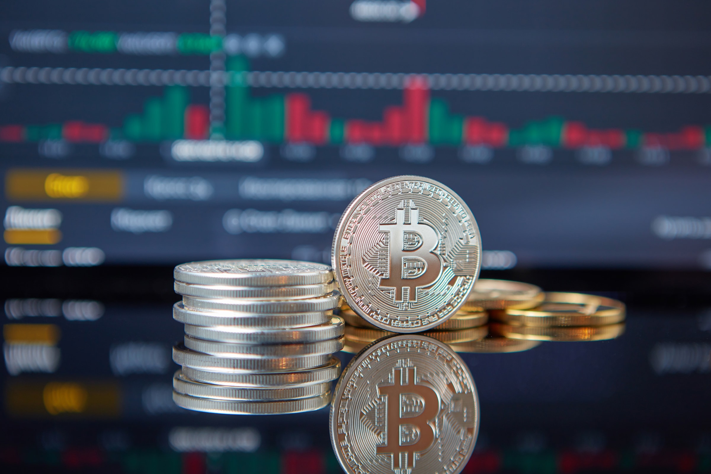 Stack of Bitcoin coins in front of a stock market graph, reflecting cryptocurrency trends.