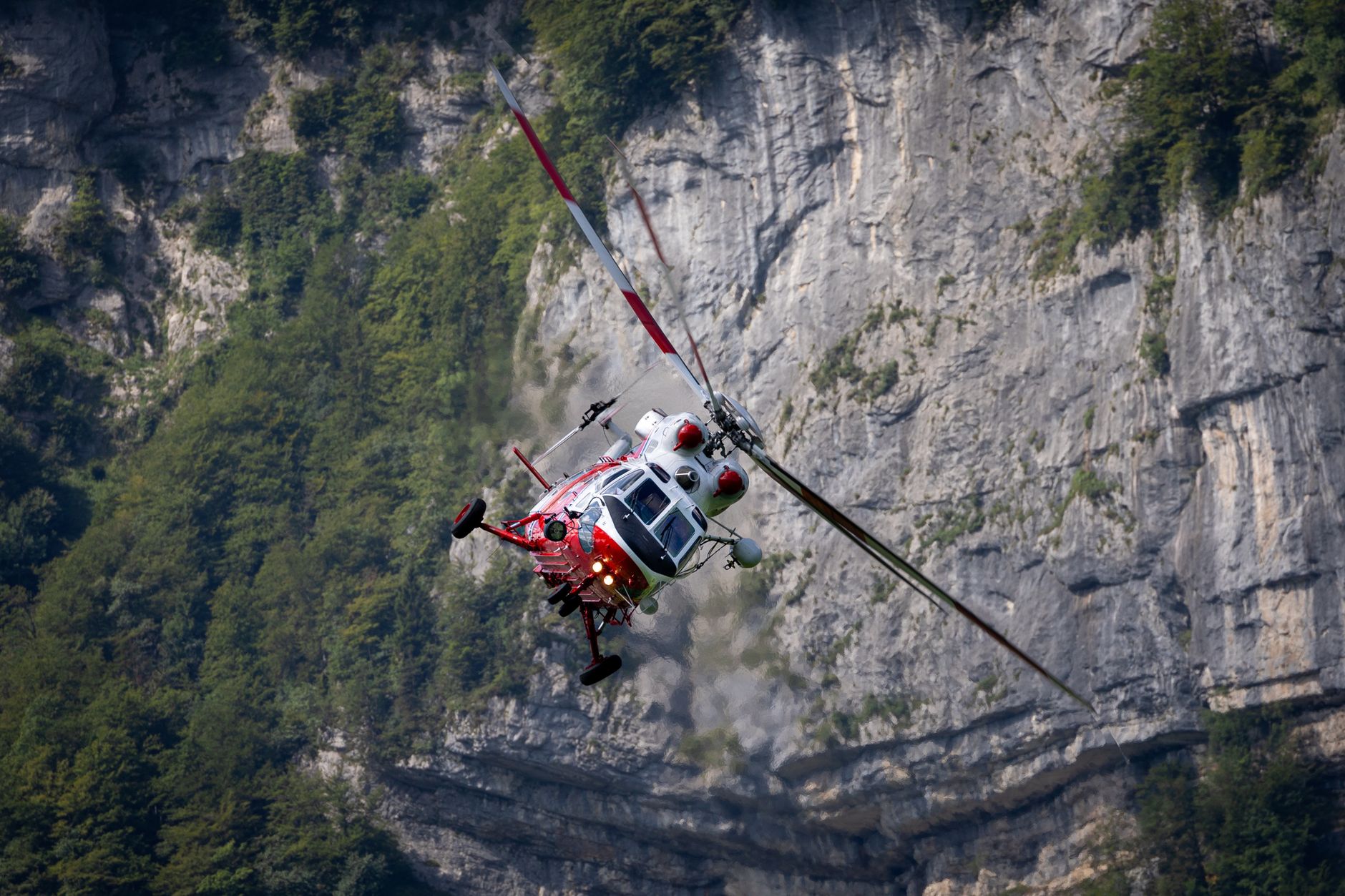 A rescue helicopter maneuvers near the rocky cliffs of Glarus Nord, Switzerland.