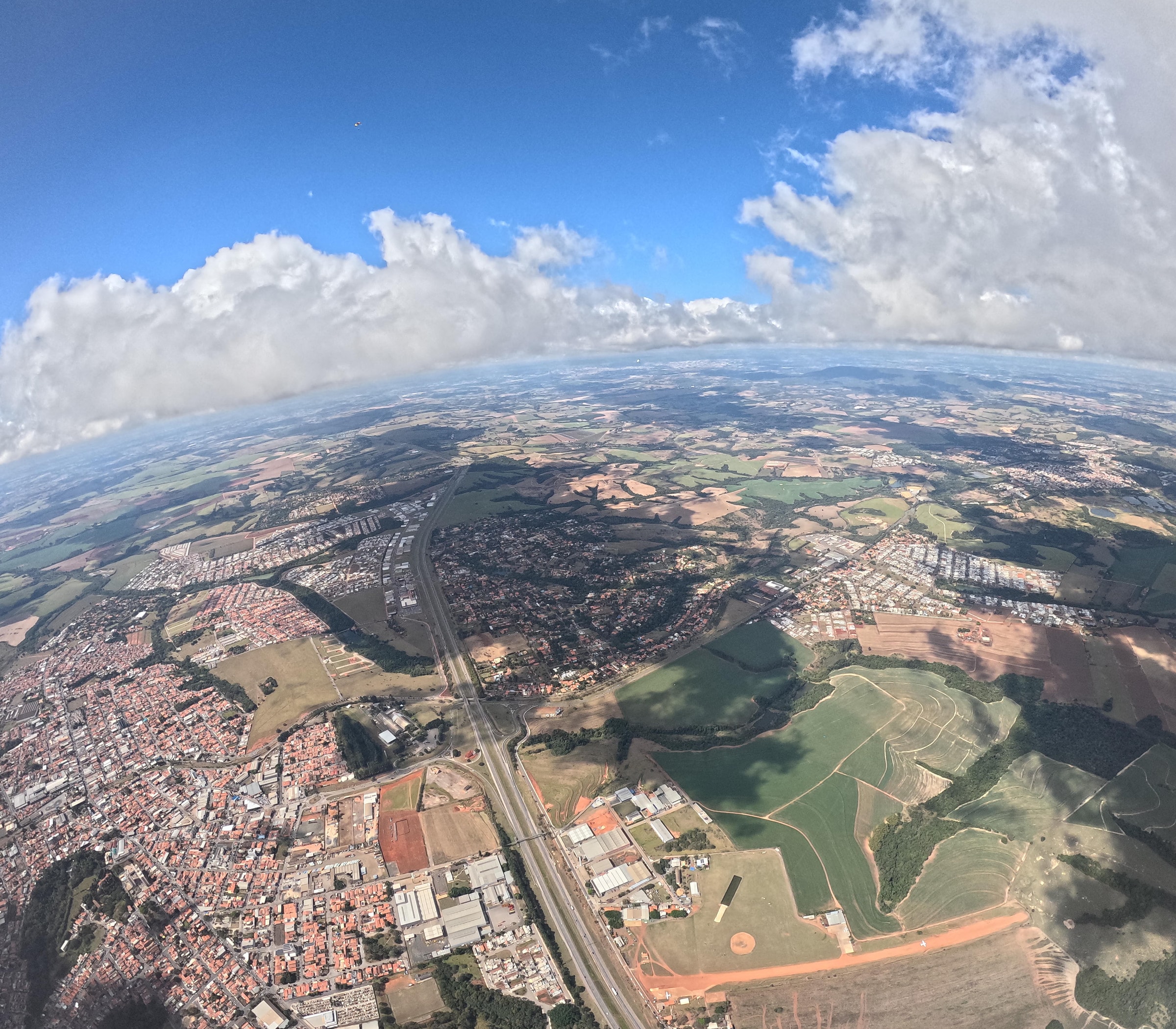 Expansive aerial view of a countryside cityscape under a vibrant blue sky with fluffy clouds.