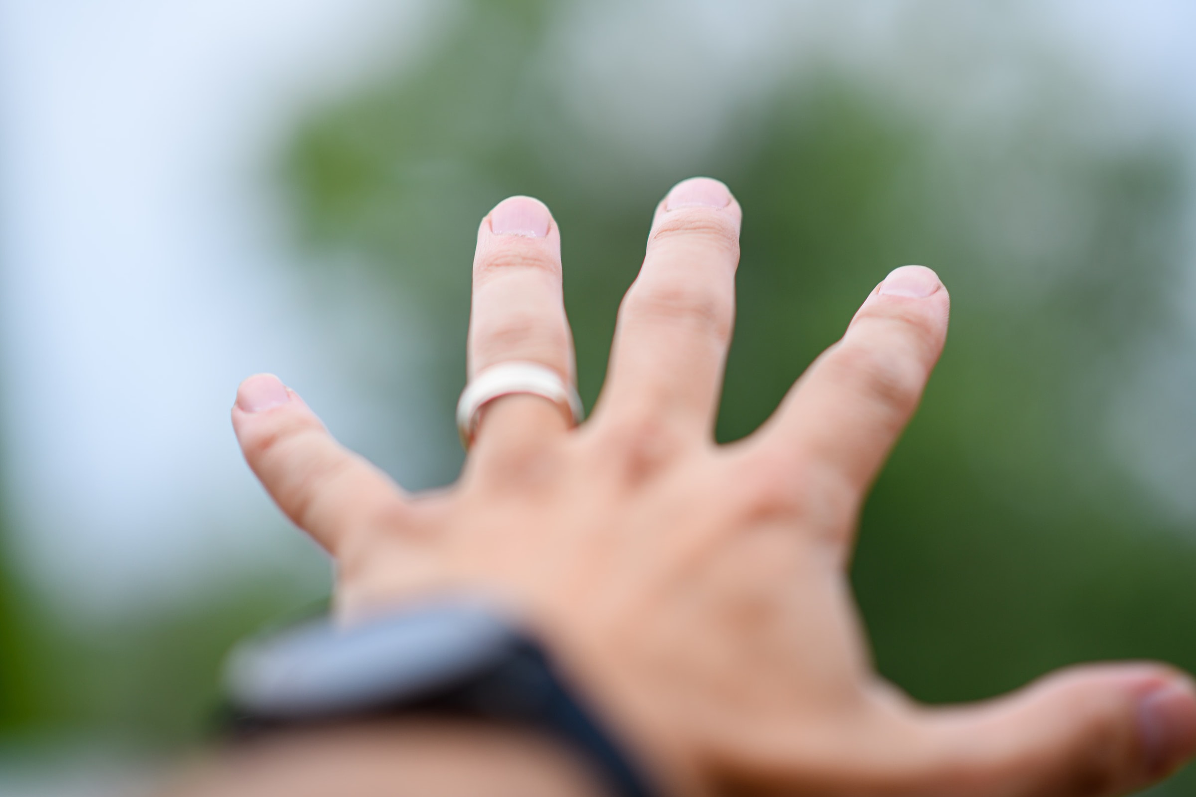 Blurred hand reaching forward with a ring on a finger, outdoors.